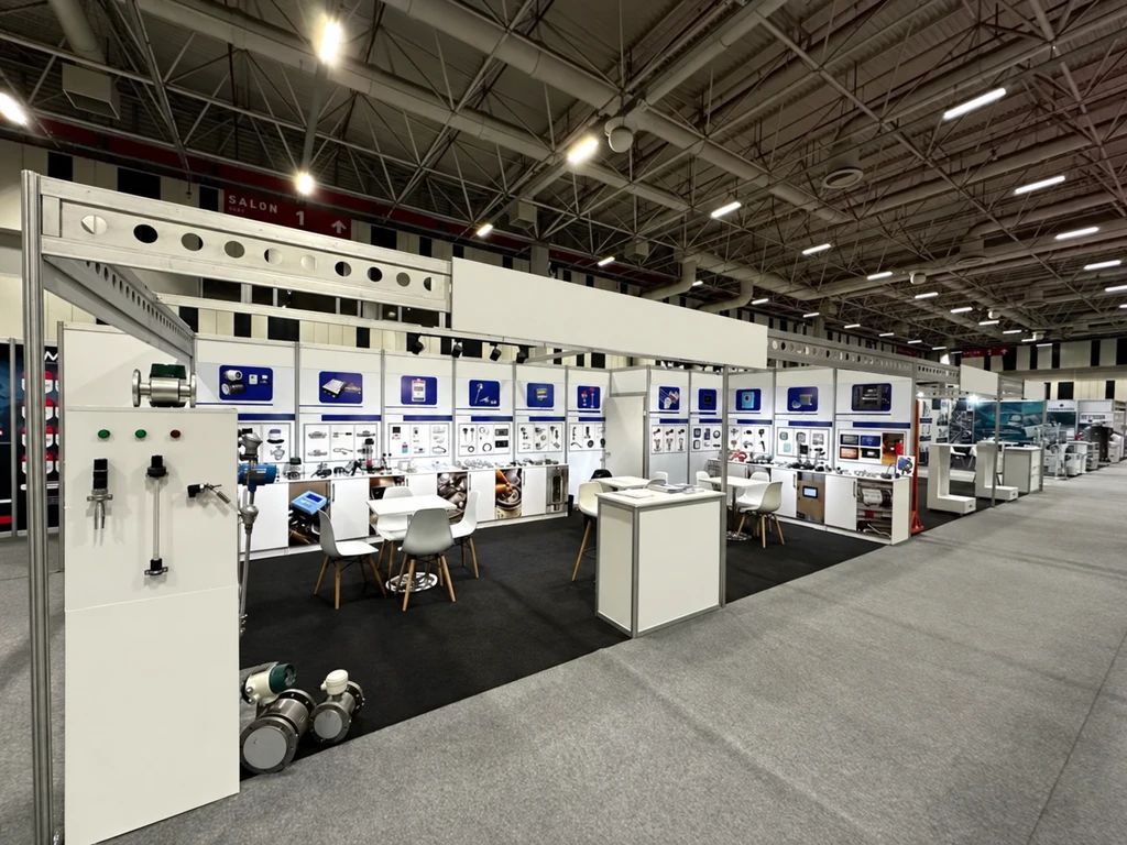 Full industrial exhibition booth with large-format technical panels and a visitor seating area